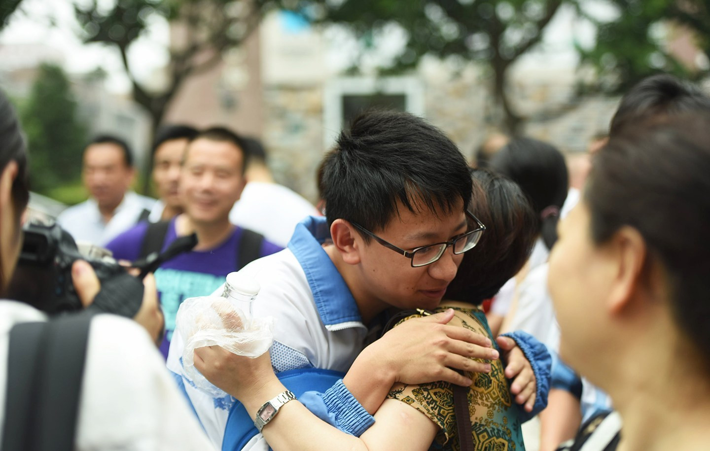 考场内是"战场",考场外也不轻松,考生家长在考点外刷手机,看报纸,烈日