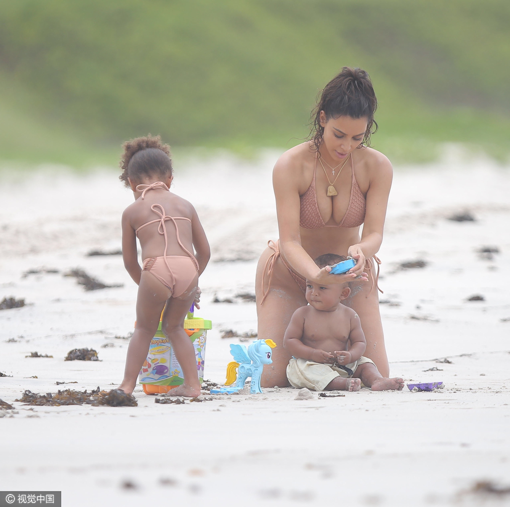 当地时间8月18日，金·卡戴珊（Kim Kardashian）带女儿小西北和儿子沙滩玩耍，卡戴珊身穿裸色系带比基尼，女儿与妈妈同款可爱十足，在沙滩上卡戴珊全程呵护幼子母爱爆棚，然而抢镜的还是翘臀。图为卡戴珊把玩玩具。
