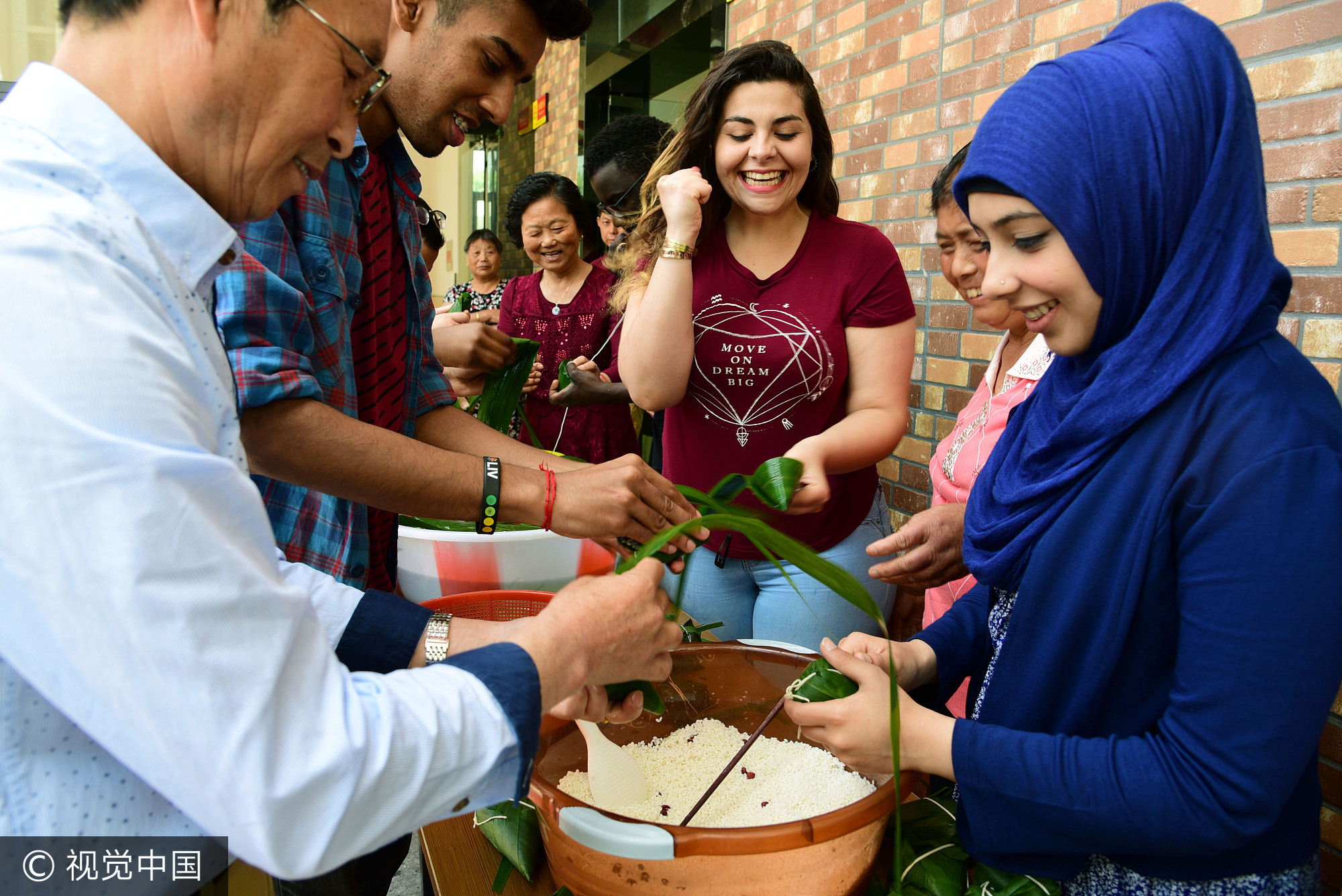 2017年5月25日,江苏镇江,社区居民在指导外国留学生包粽子。当日,端午节临近,江苏大学十多名来自赞比亚、印度、土耳其、巴基斯坦、南非等国的留学生走进镇江市和平路街道金江社区,在居民指导下学习包粽子、缝香囊,在咸鸭蛋上描画端午民俗,体验中国传统的端午文化。
