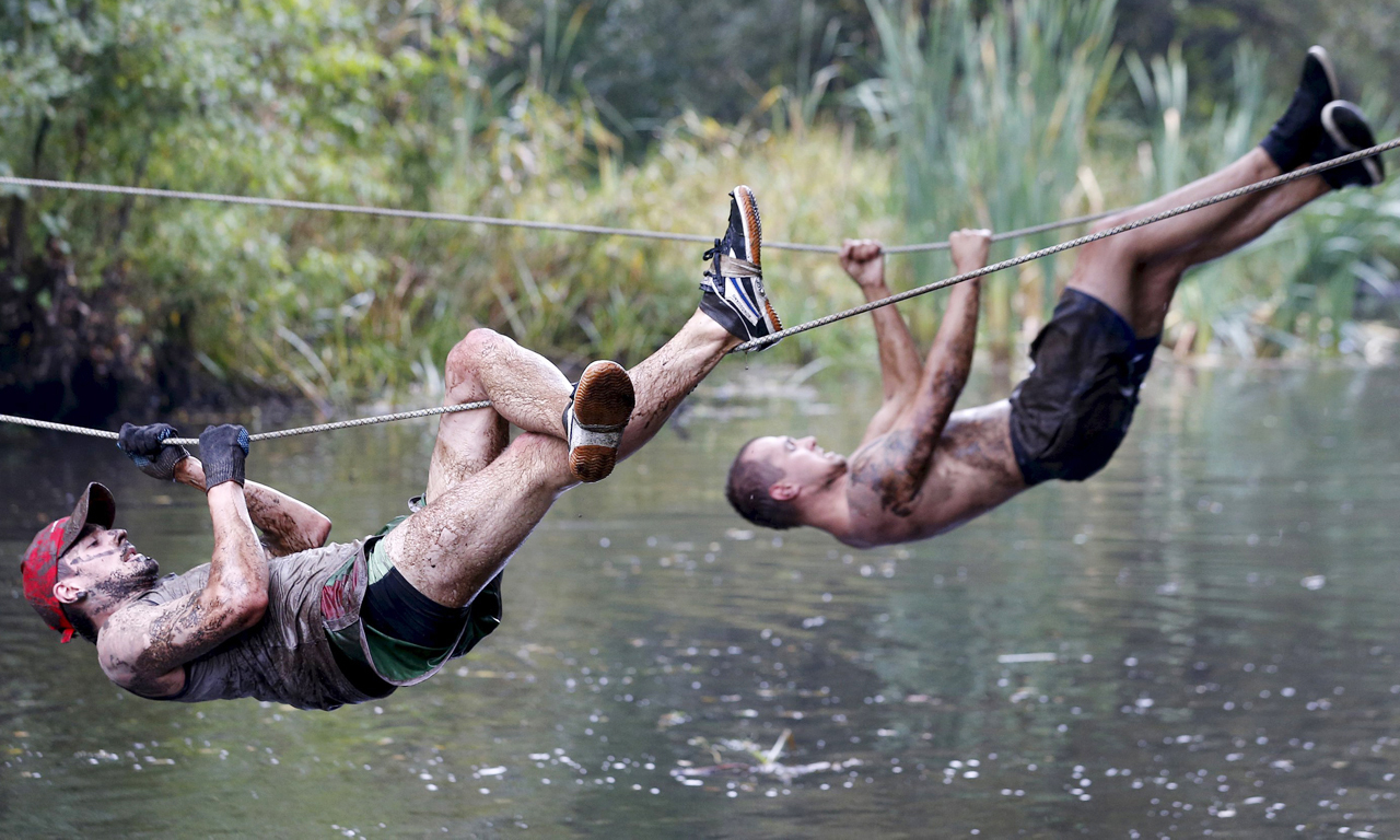 泥浆穿越（Tough Mudder）是一个10到12英里障碍赛，它相当的艰苦，比赛中经常会出现骨折甚至是断腿的事件。图为选手爬铁丝穿越河流。
