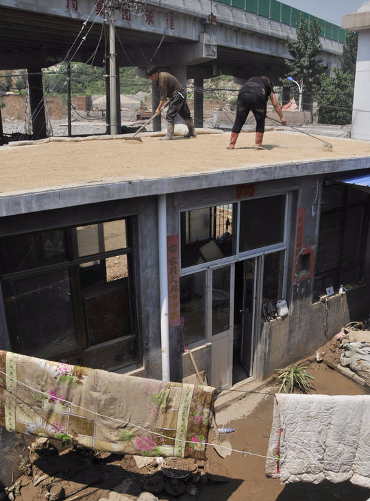 7月23日，井陉县小作镇南石门村村民赵红新（左）在屋顶晾晒小麦。他家2000多斤小麦被冲得只剩五六百斤。新华社记者 巩志宏 摄