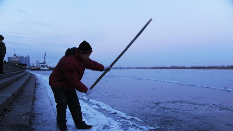 清晨，哈尔滨冬泳协会会员们用木棍凿开冰面，进入松花江冬泳。