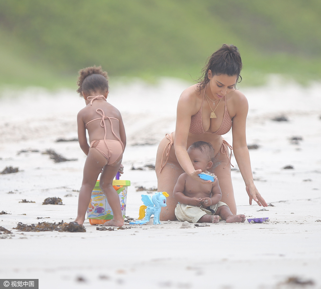 当地时间8月18日，金·卡戴珊（Kim Kardashian）带女儿小西北和儿子沙滩玩耍，卡戴珊身穿裸色系带比基尼，女儿与妈妈同款可爱十足，在沙滩上卡戴珊全程呵护幼子母爱爆棚，然而抢镜的还是翘臀。图为卡戴珊爱意浓浓教幼子。