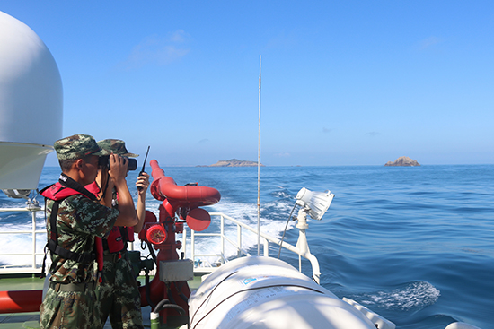 图为边防官兵通过望远镜观察无人岛屿
