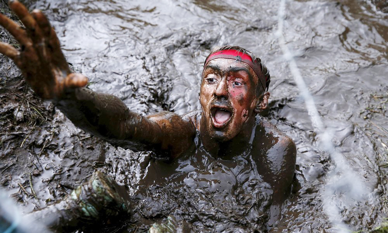 又比如掉进一个装满了冰水的垃圾箱，冲刺通过一段通有超过10000伏电压的电线的地带，还有其他具有挑战性的军事障碍。图为选手陷入泥潭。