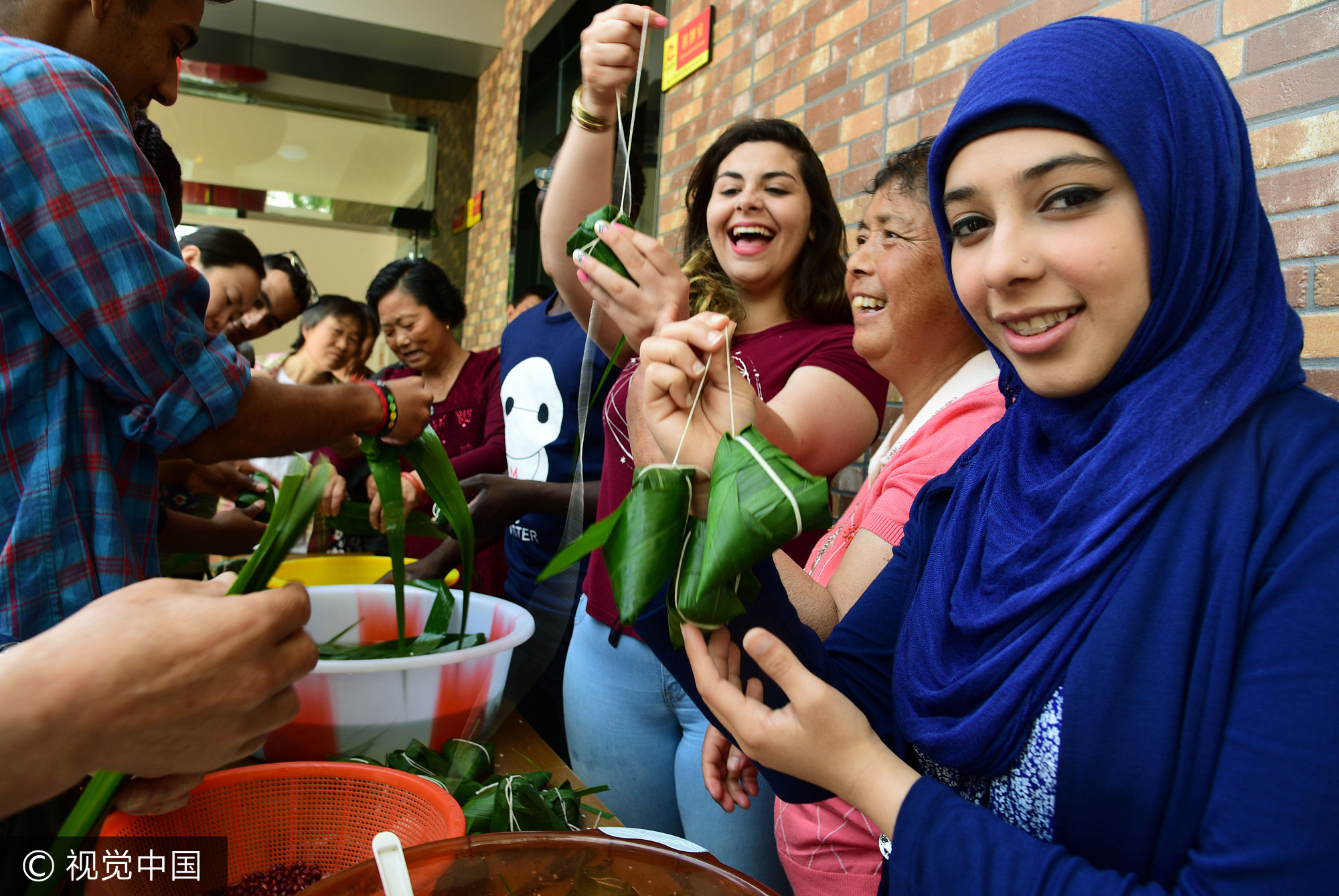 2017年5月25日,江苏镇江,社区居民在指导外国留学生包粽子。当日,端午节临近,江苏大学十多名来自赞比亚、印度、土耳其、巴基斯坦、南非等国的留学生走进镇江市和平路街道金江社区,在居民指导下学习包粽子、缝香囊,在咸鸭蛋上描画端午民俗,体验中国传统的端午文化。